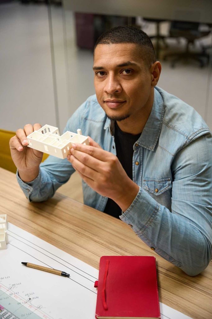 Cheerful man sitting at table and holding building prototype